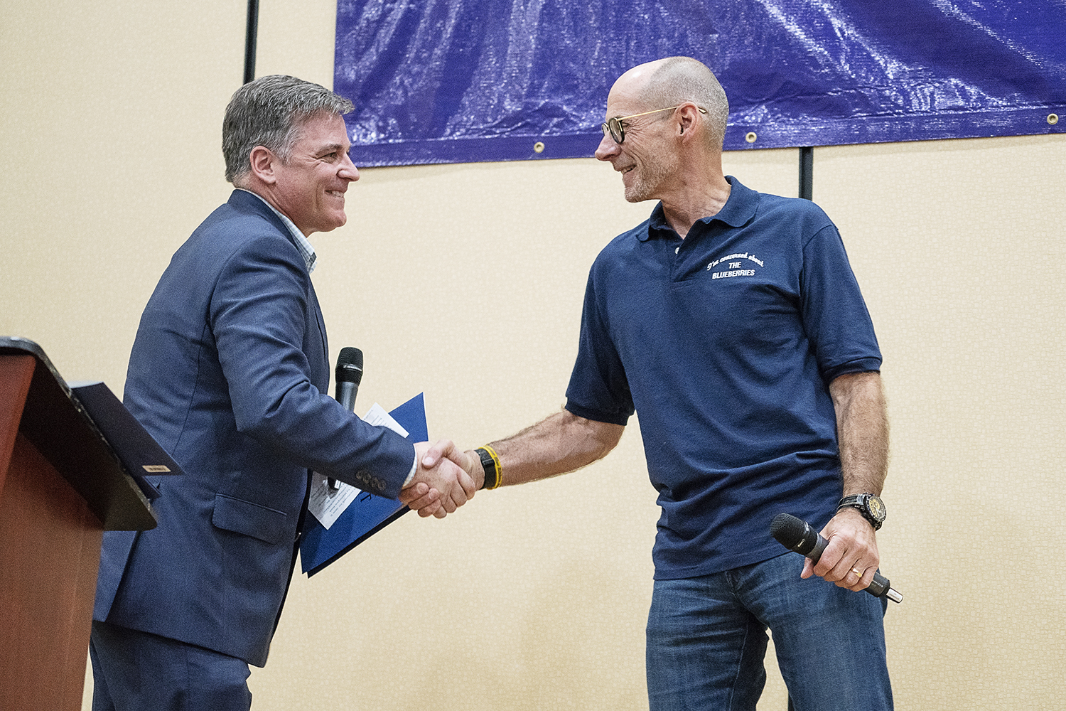 Flint, MI - Friday, May 4, 2018: Blueberry Founder and Fenton Twp. resident Phil Shaltz (right), 69, shakes hands with Greg Viener, Community President for Huntington National Bank as he takes the stage during the 5th Annual Blueberry Ambassador Awar