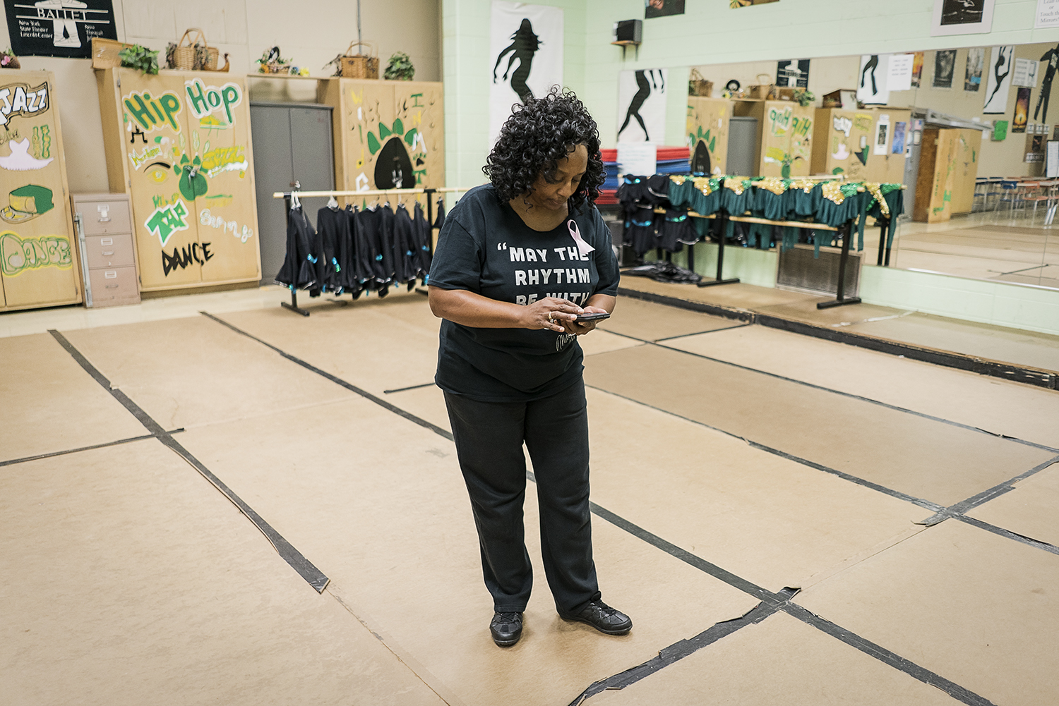 With work still to be done, Sheila Miller-Graham checks her phone while on the dance floor of her classroom at Flint Northwestern High School. Miller-Graham wears many hats between the high school, her dance studio and her church. She considers givin