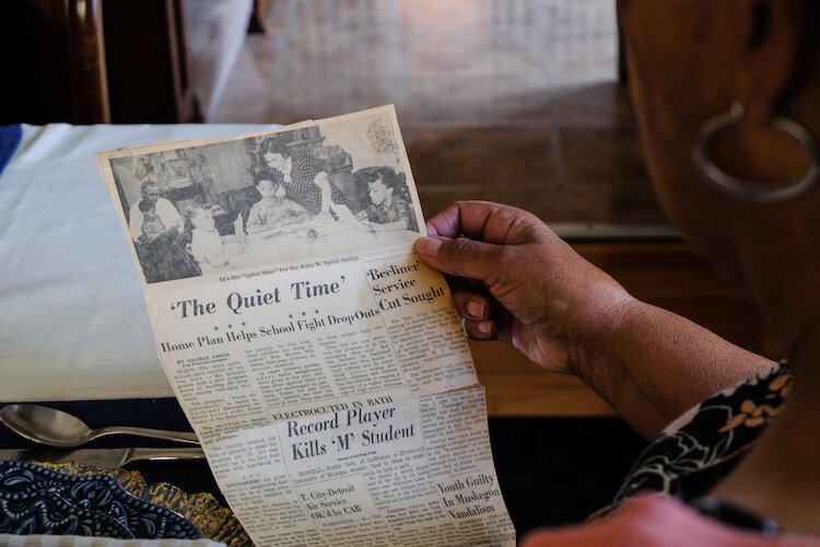 Raynetta holds a 1961 Detroit Free Press education article showing the Speed family in their dining room during an evening after school.