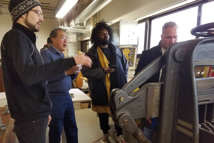 Matthew Osmon, a Mott Middle College instructor who head's up Factory Two's flat stock silk screening area, demonstrates a 1920s industrial paper cutter for Jon Hardman, Yo-Yo Ma, and Tunde Olaniran. 
