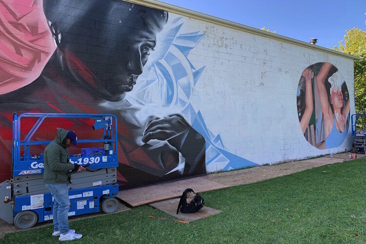 Muralist easeone_tx prepares to continue his mural on Oakley Street for Flint's Free City Mural Festival.