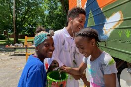 Aniyah Colston, 13; Isaiah Crockett, 16; and Aniyah Colston (left to right) giggle before the camera while painting a mural on the water distribution trailer in the Joy Tabernacle parking lot.