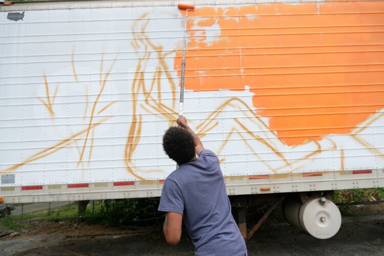 Cedreon Chapman, 16, applys an orange back drop to the water distribution trailer mural during a Friday morning paint session.