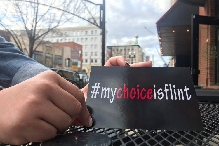 Kristin Stevenson, of the City of Flint’s Planning and Development office holds a sign for the Flint Choice Neighborhoods Initiative, in downtown Flint.