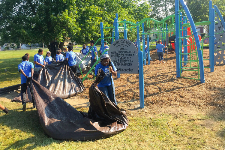 Volunteers use tarps to haul wood chips to mulch the area around the playground.