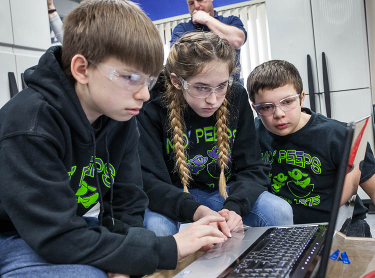 Alex Wickham, 13, (left); Lydia Minzey, 12; and Parker Oosterhof, 12, (right) work to program a robot for competition. The students are members of the Carman-Ainsworth Middle School team traveling to Louisville, Kentucky for the world robotics champi