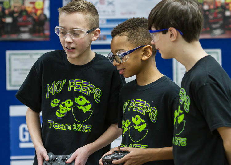 Caleb Rose, 13, (left); Micah Shamly, 12; and Jack Roy, 12, (right), all students at Carman-Ainsworth Middle School, demonstrate driving the robot and picking up objects. The students are members of the Carman-Ainsworth Middle School team traveling t