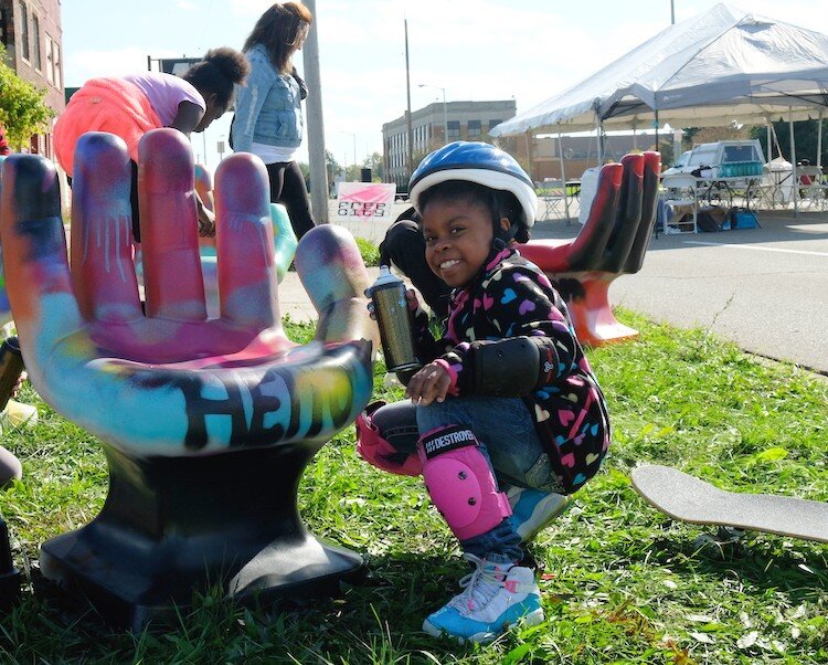 Zameena Brown, 8, poses with one of the spray painted chairs at Flint's Free City Mural Festival on Saturday, Oct. 12, 2019.