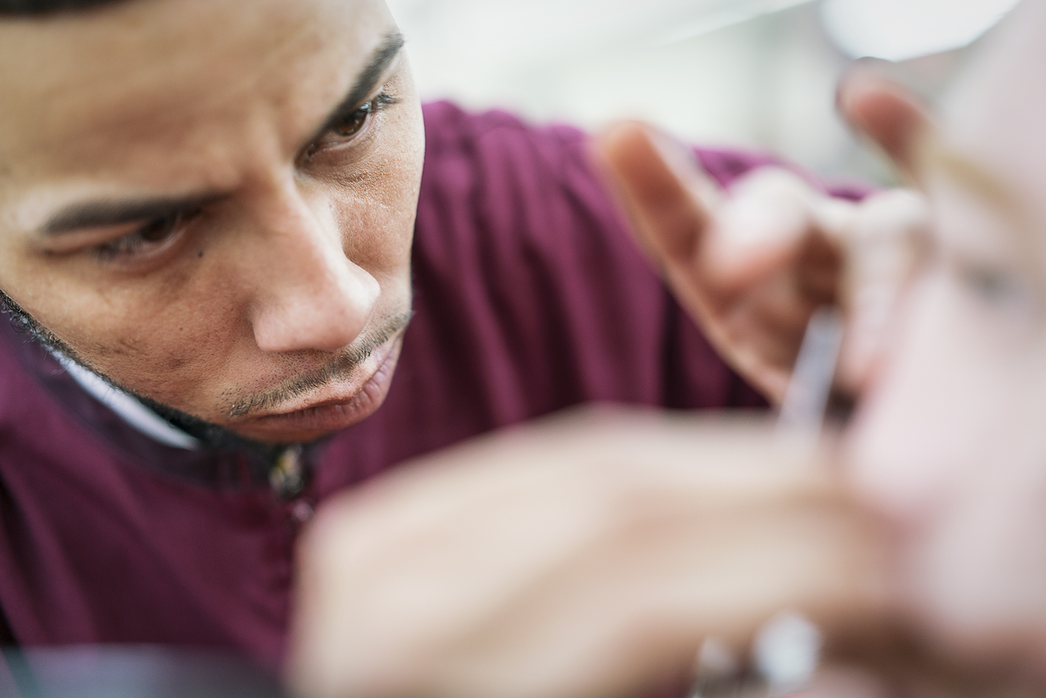 Flint, MI - Tuesday, February 6, 2018: Barber Nick Gallardo, 26, from Bay City, draws close to focus while he shaves the beard of Manuel Rodarte, 35, from Saginaw, another student at the Flint Institute of Barbering.