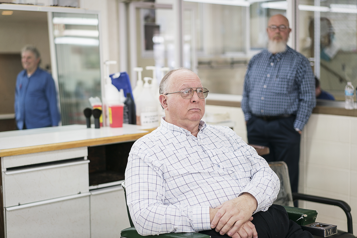 Flint, MI - Tuesday, February 6, 2018: Linden resident Larry Woodby, 70, an instructor at the Flint Institute of Barbering, sits in an empty chair flanked by the reflection of Bob Morey, 68, from Linden, Director of Education (left) and Ted Taylor, 6