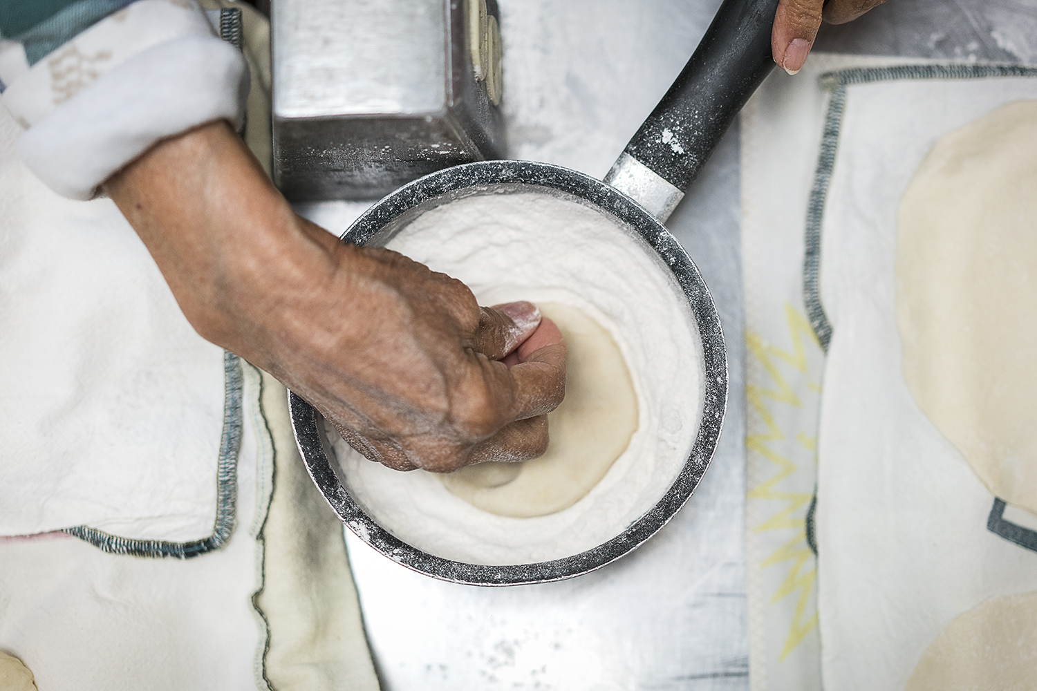 Lupita Vargas, 87, of Flint, gently places masa into a small pot of flour, tapping a couple times each side for a nice, even coat before rolling it out to make a tortilla.