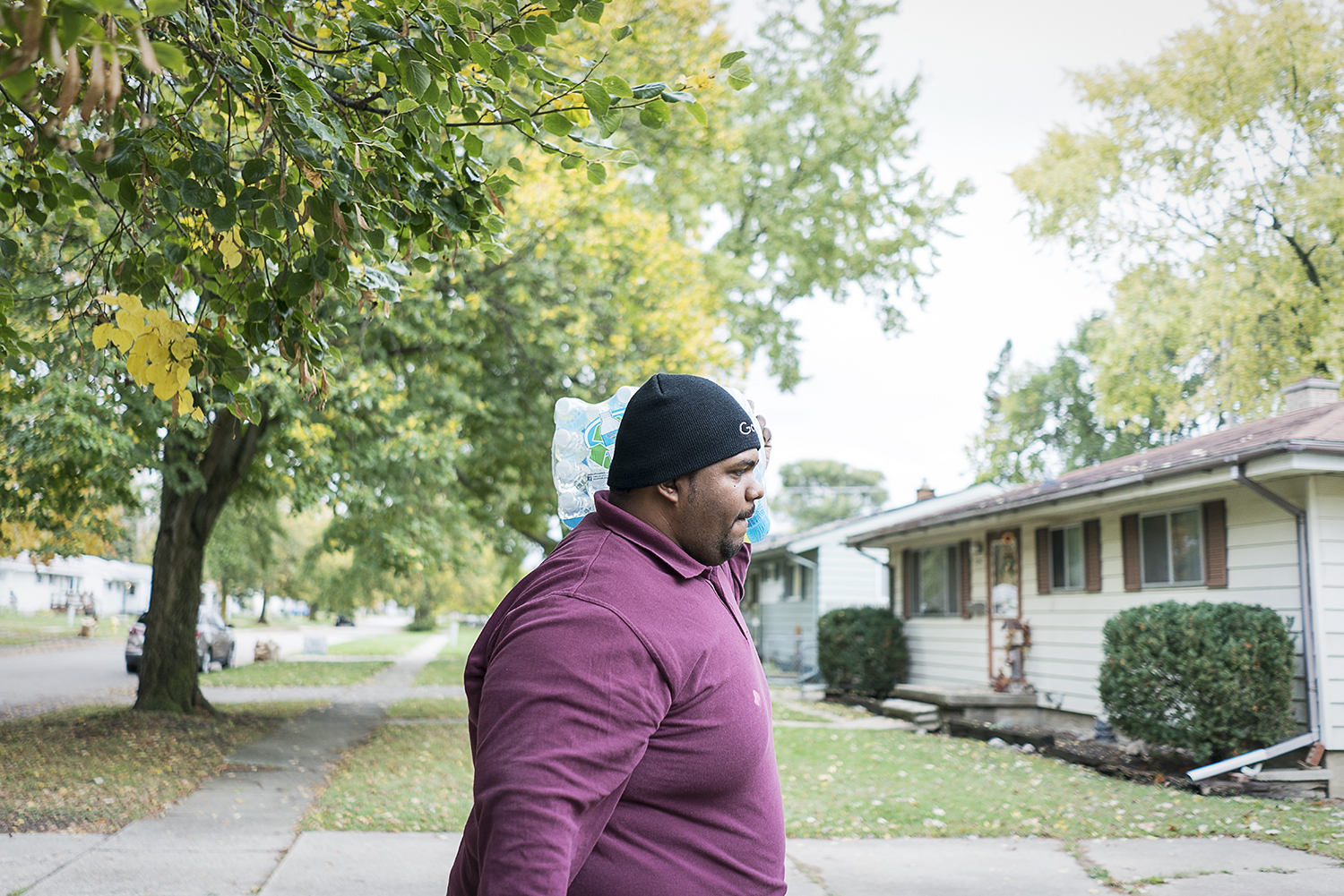 With a case of water bouncing on his shoulder, Flint resident William Harris, 31, walks up the sidewalk to a home on the eastside of Flint. 