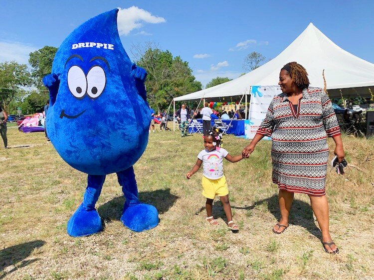 Ruth Harrison with her granddaughter Sarai Mitchell, 3 walking alongside Drippie the mascot at the 2nd Flint Town "Back to School" Carnival Splash.