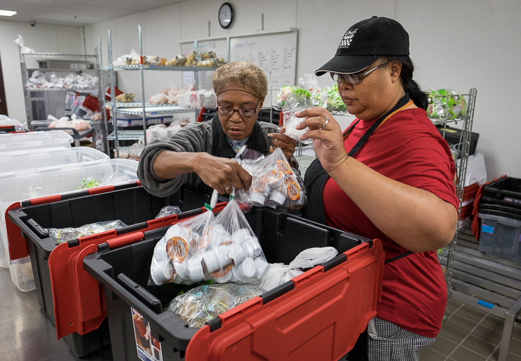 Food service associates Petenia Atkins (left) and Kimberly Williams load crates of food in the production kitchen at the Food Bank of Eastern Michigan in Flint.