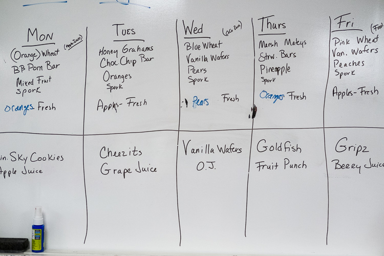 A white board details the schedule of snacks that will be distributed. The board is on a wall in the production kitchen at the Food Bank of Eastern Michigan in Flint.