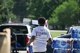 A young volunteer hands out packs of bottled water to community members.
