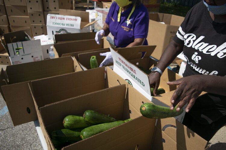 Two volunteers sift through boxes filled with vegetables while putting together care packages for community members.