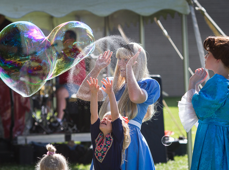 Ashley Grovesteen as "Alice" and Elizabeth Timm (right) as "Wendy Darling" react as a child bursts a bubble at the 8th Annual Miracle Picnic at the Sloan Museum. 