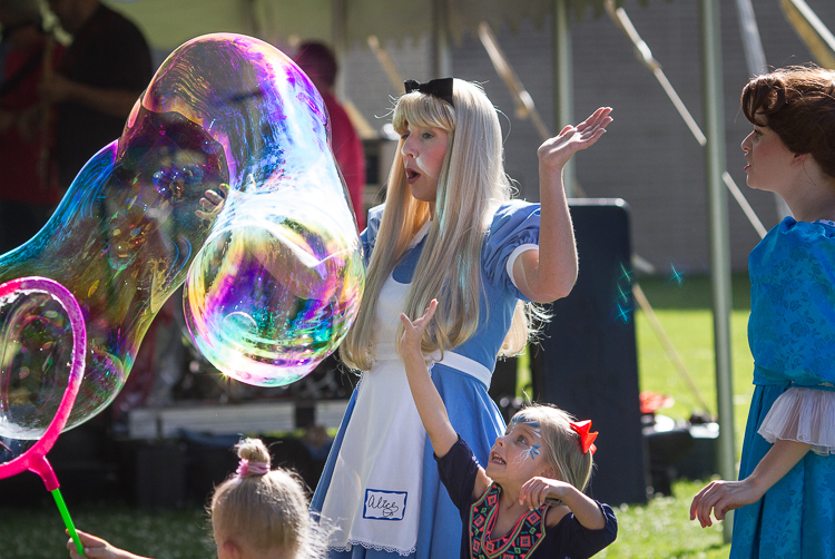 A child reaches to burst a bubble at the 8th Annual Miracle Picnic at the Sloan Museum on Tuesday.  Ashley Grovesteen as "Alice" and Elizabeth Timm (right) as "Wendy Darling" play with the children just before the bubble bursts. 