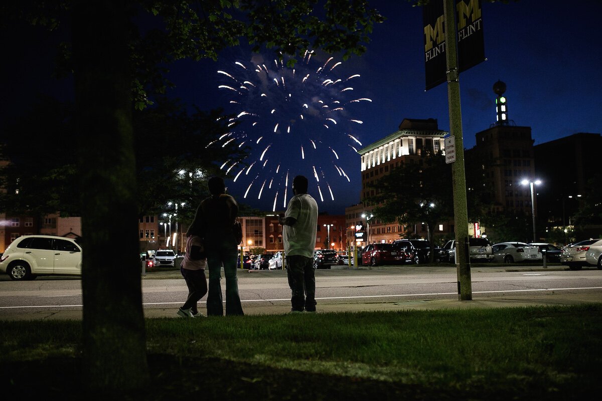 Fireworks go off overhead as people walk downtown Flint on Juneteenth.