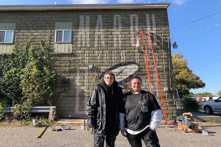 Returning muralists Nomad Clan stand before their mural in progress on the side of the Golden Leaf during Flint's Free City Mural Festival on Saturday, October 12, 2019.