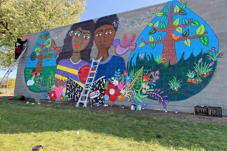 Muralist Magda Love signs her initials on her mural at the International Academy of Flint during the Free City Mural Festival.. 