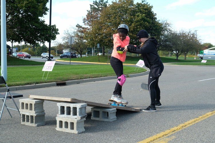 Nyerah Colen, 10, rides a skateboard with assistance from Jenna Bankston of Brush Alley Skate Shop during Flint's Free City Mural Festival≥