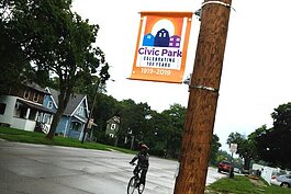 A child bicycles past one of the orange signs on Dayton Avenue celebrating Civic Park's centennial. 