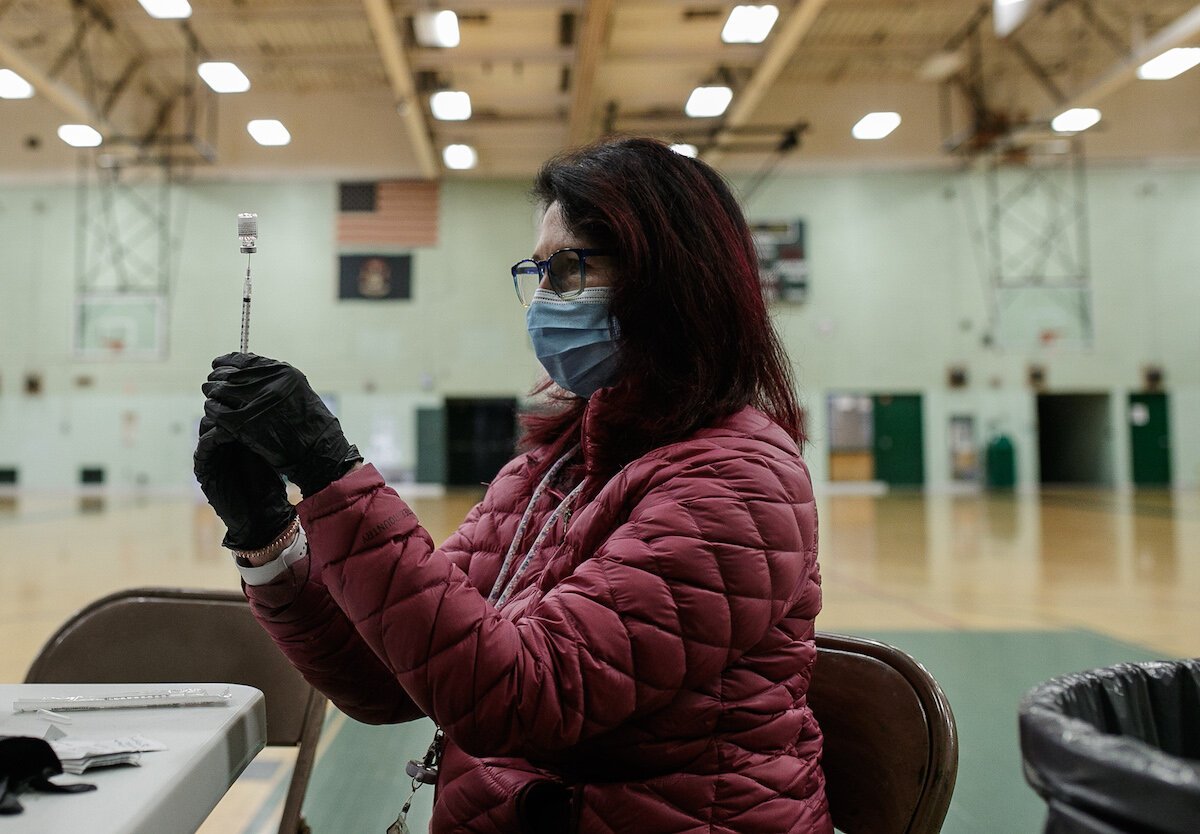 A GCHD nurse verifies the dose of a Pfizer vaccine inside NWHS gymnasium.